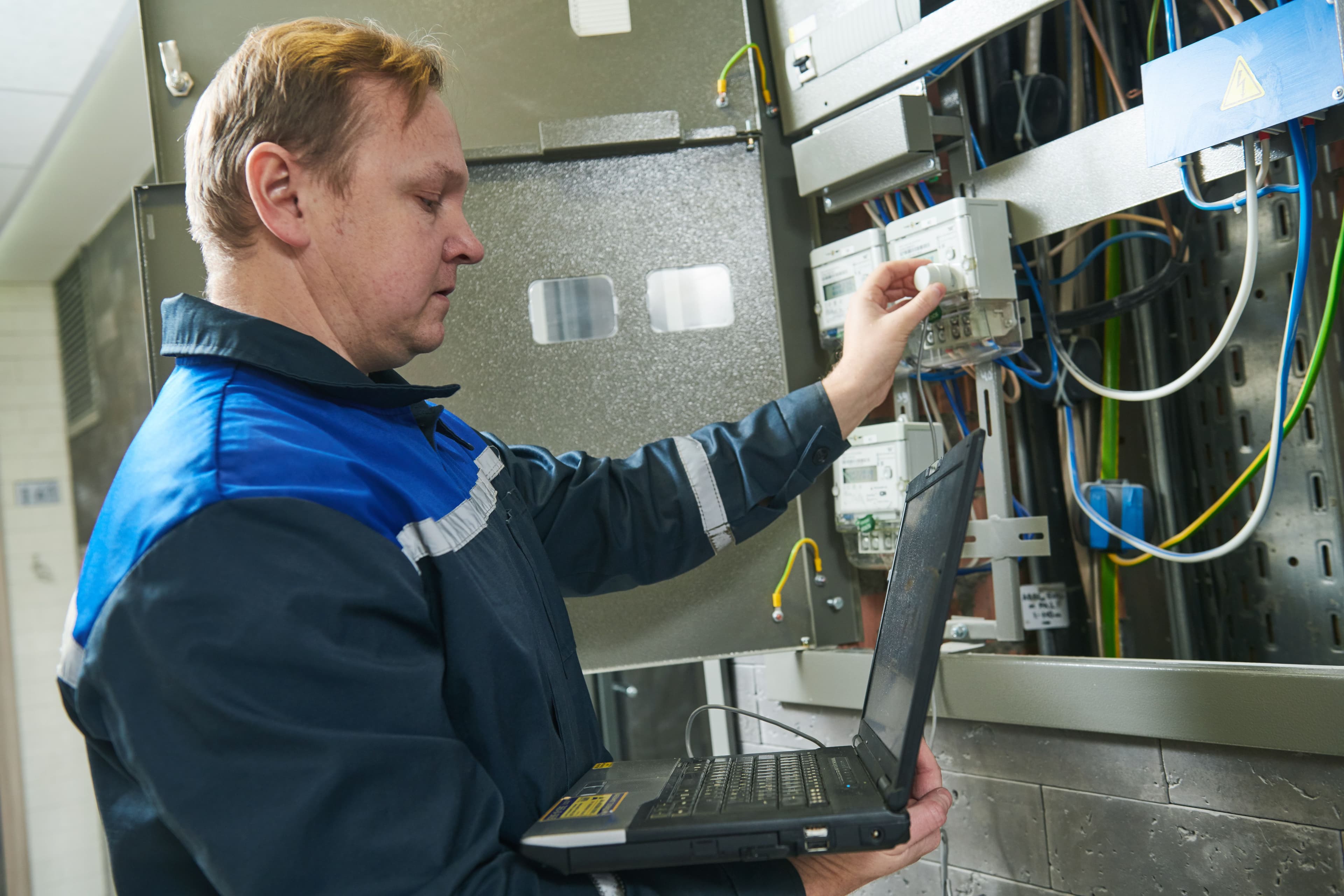 Electrician using a laptop while inspecting electrical work