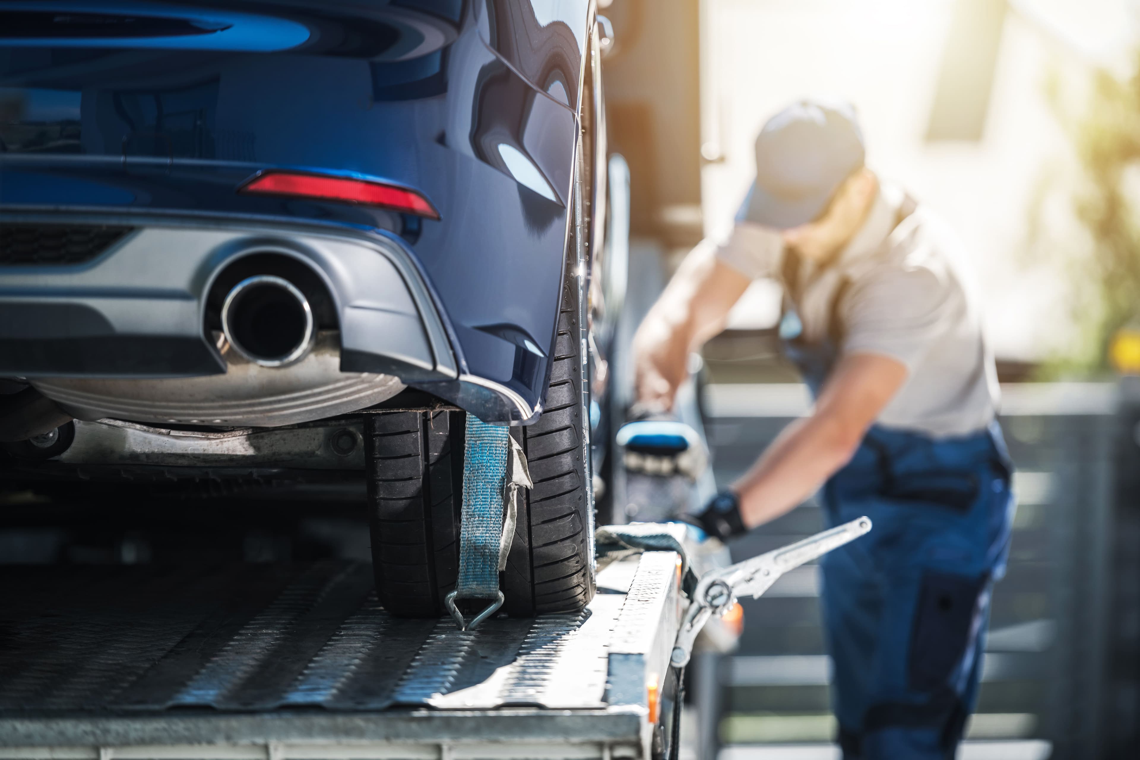 A person strapping down a vehicle on the back of a car transporter