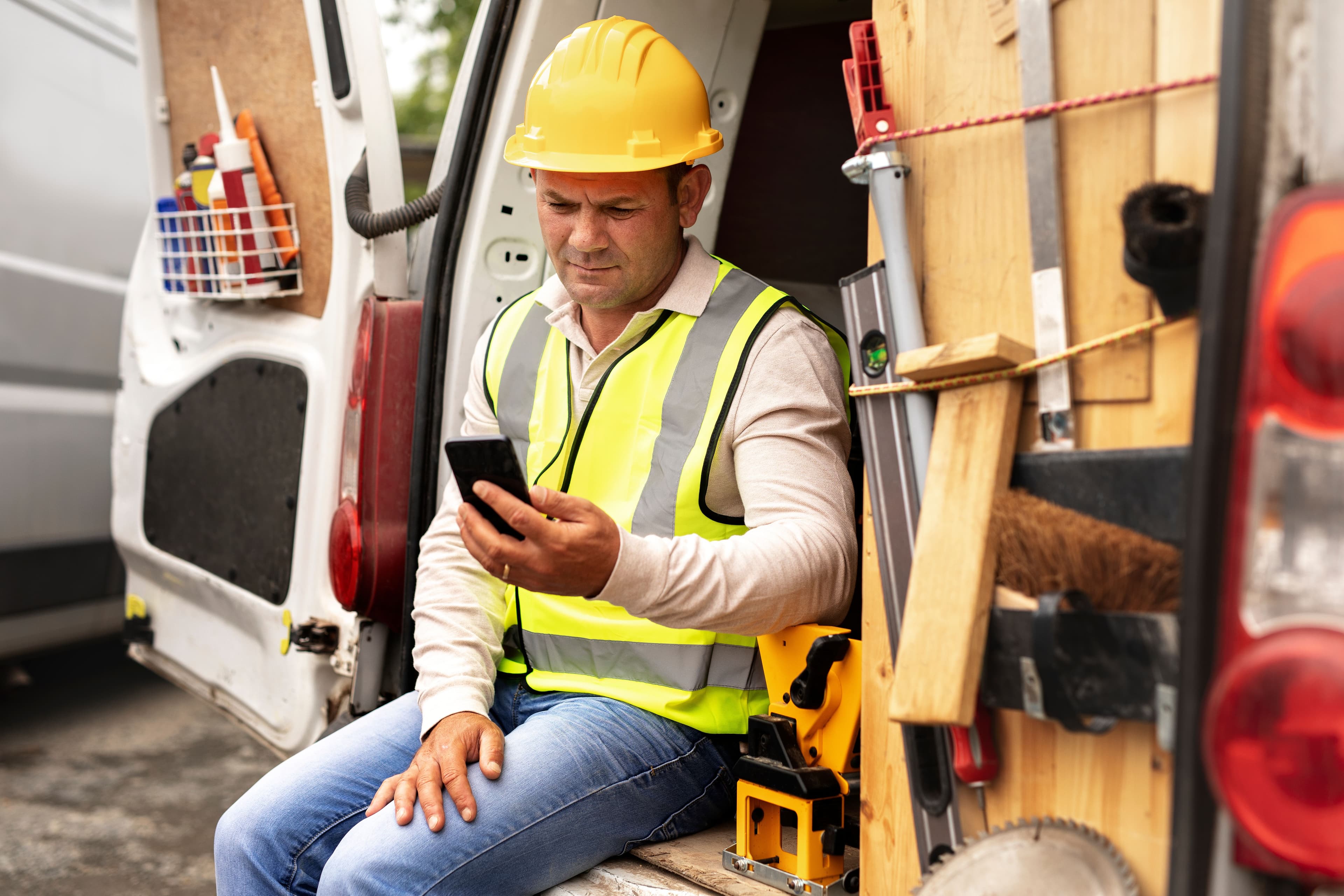 Tradesperson sitting on the back of their van while using a phone