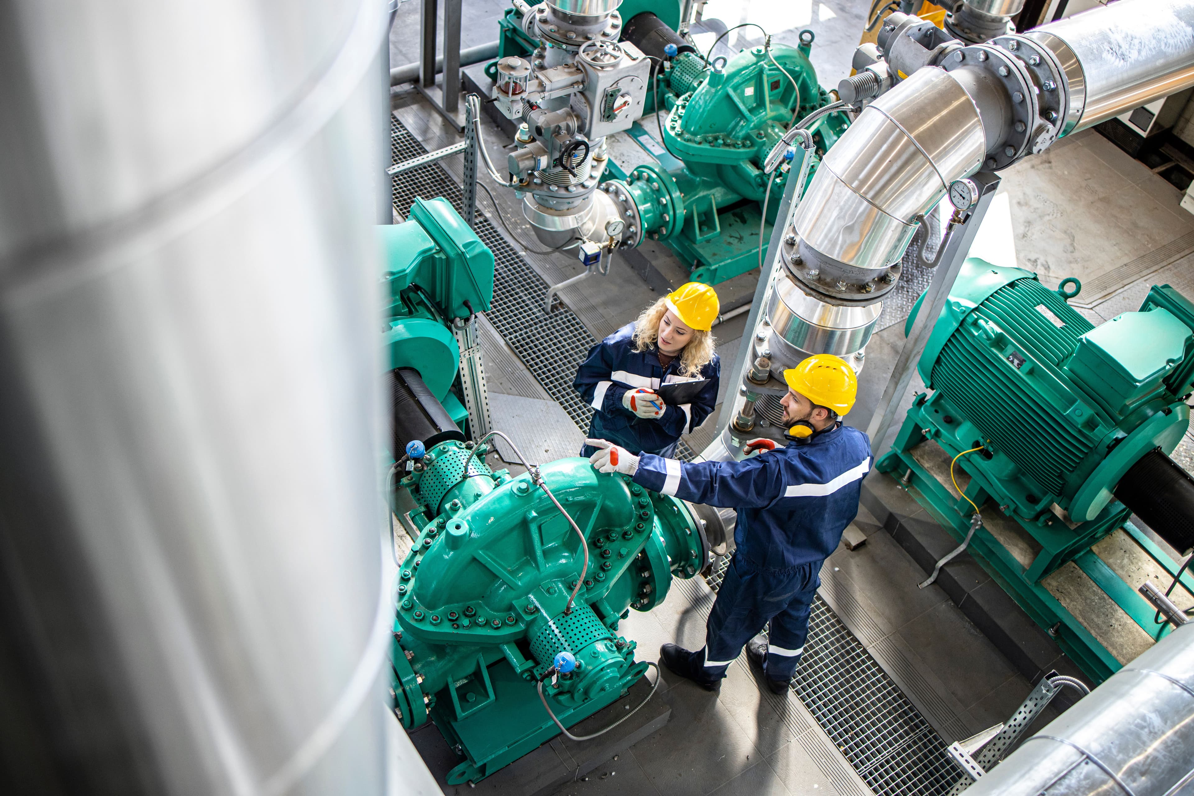 Two people wearing protective clothing while pointing at a industrial generator 