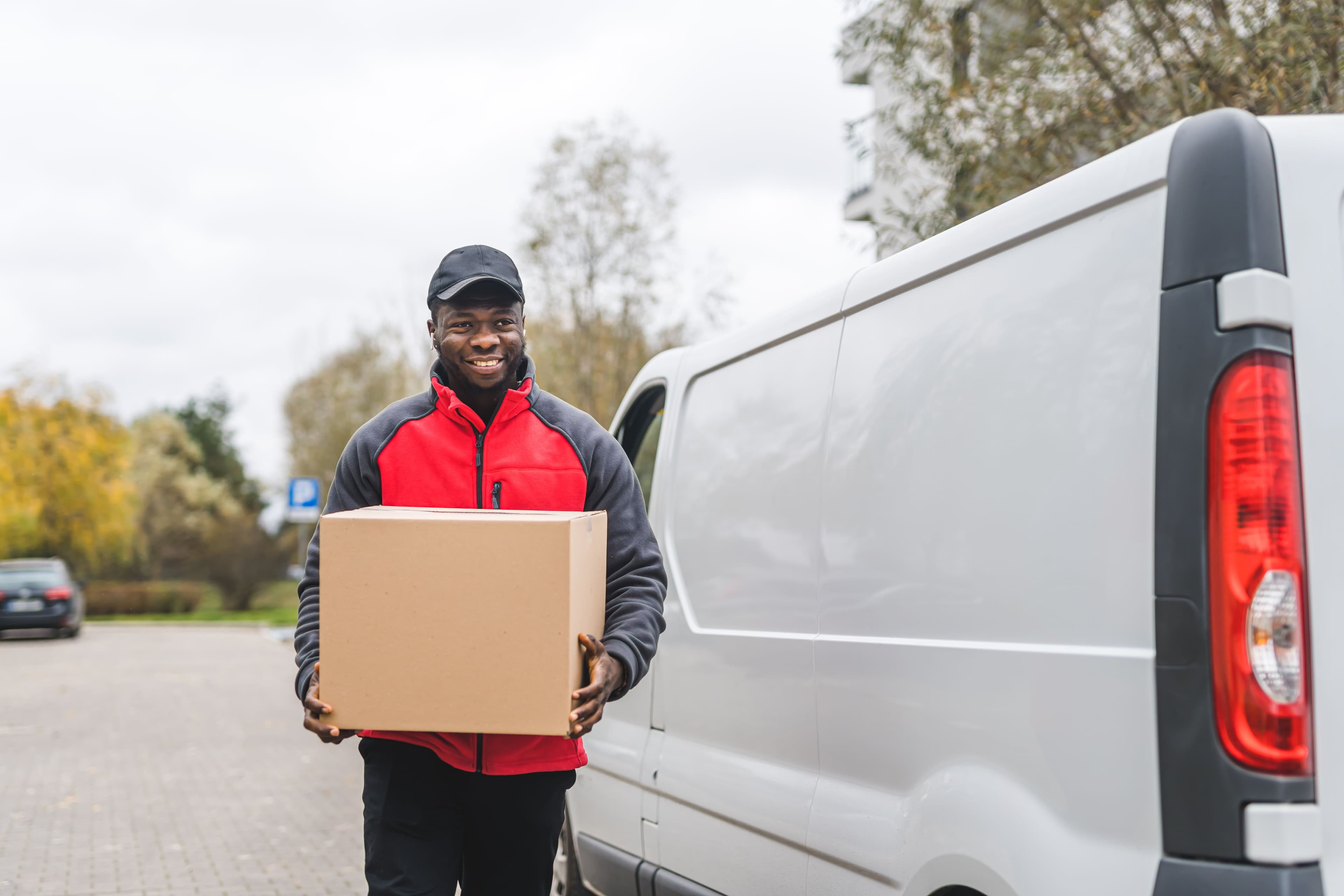 A courier driver walking away from a van holding a parcel in their hands