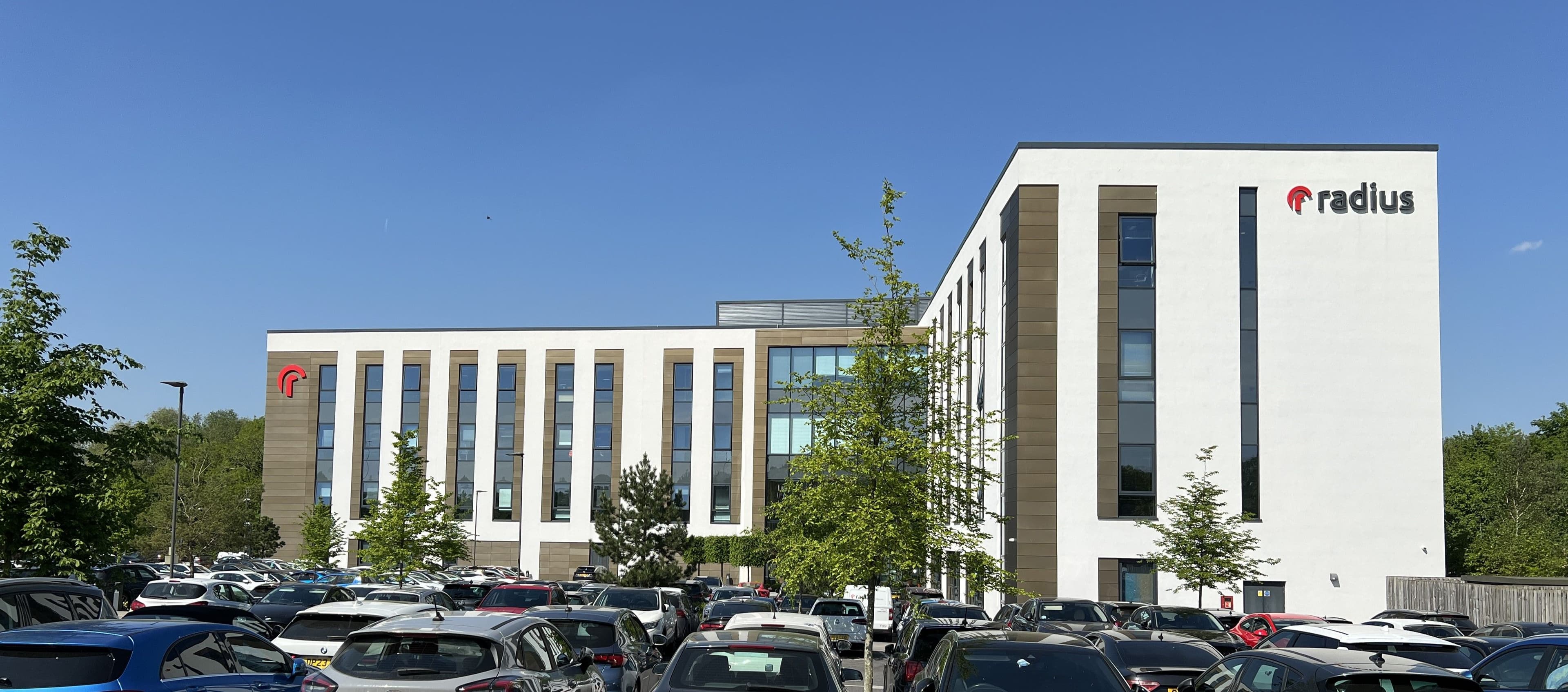 Large building on a sunny day, some cars in car park at the bottom of the photo