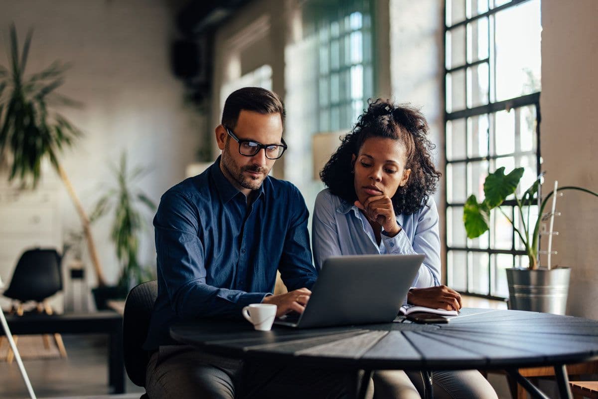 Two people sitting down at a table having a business meeting while looking at a laptop