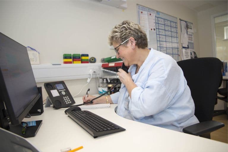 Women sat down at a desk, holding a wired phone to her ear, whilst writing