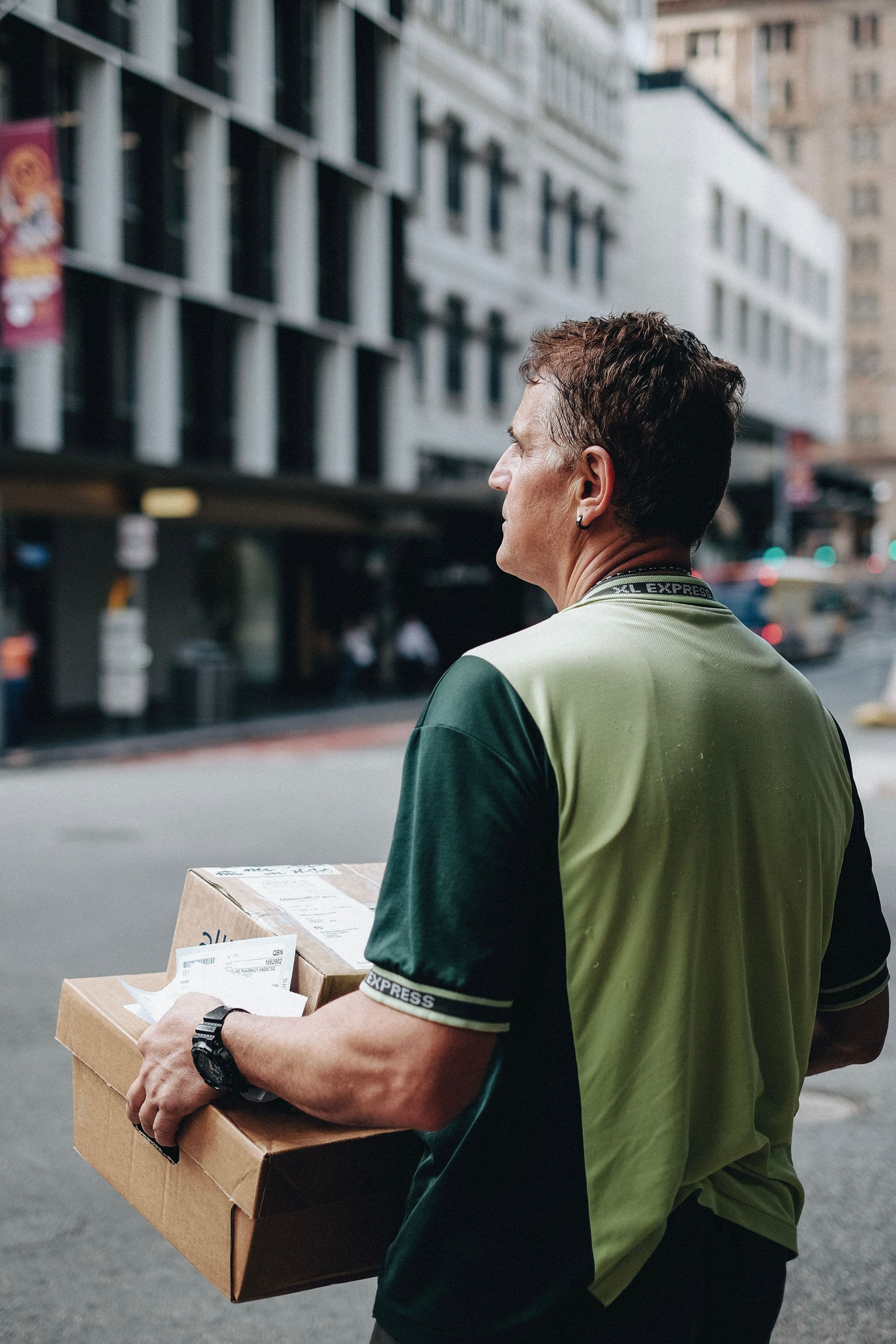 A person holding cardboard boxes waiting to cross a road