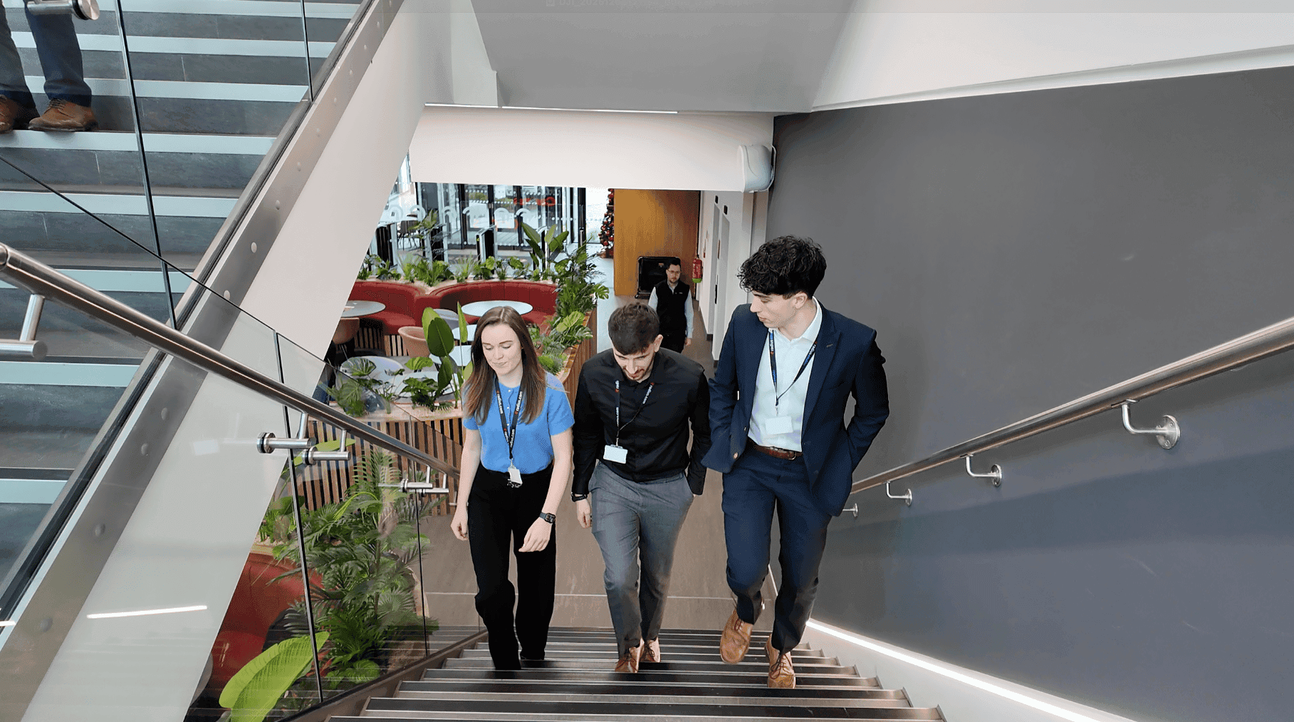 Three colleagues walking up stairs in an office with grey walls, one female colleague and two male colleagues