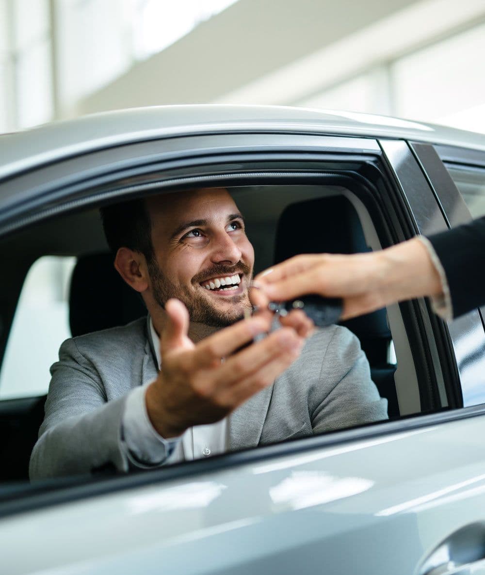 A person in their vehicle about to shake hands with someone standing outside