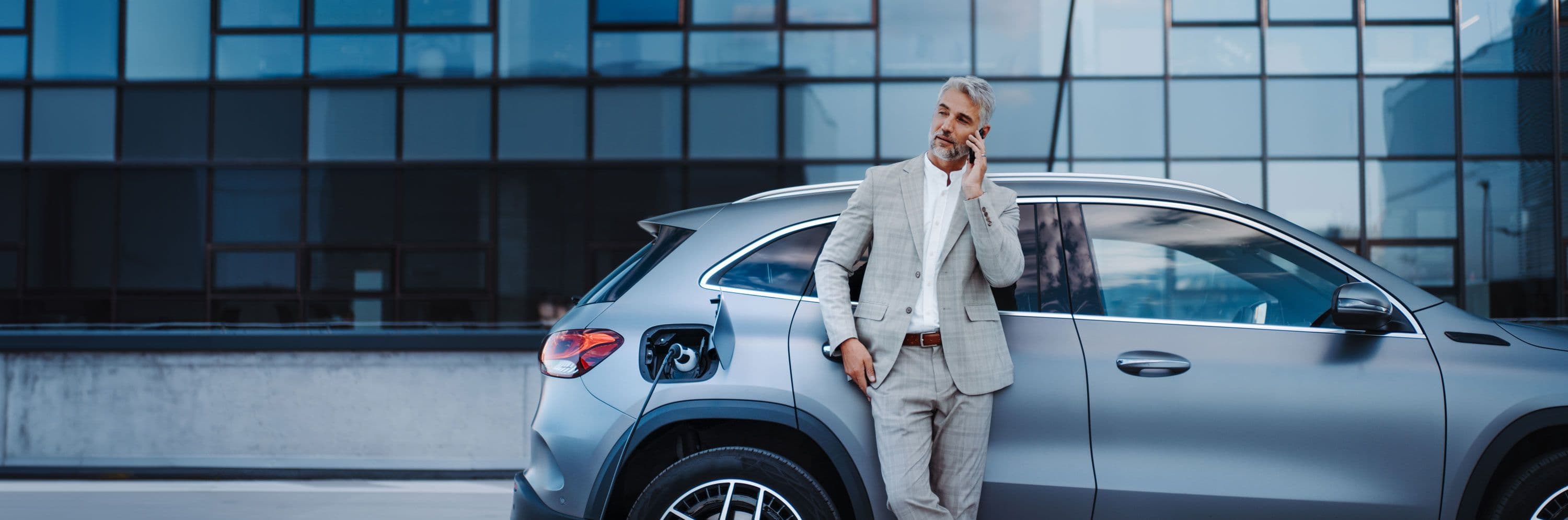 A person standing in a suit next to an electric vehicle
